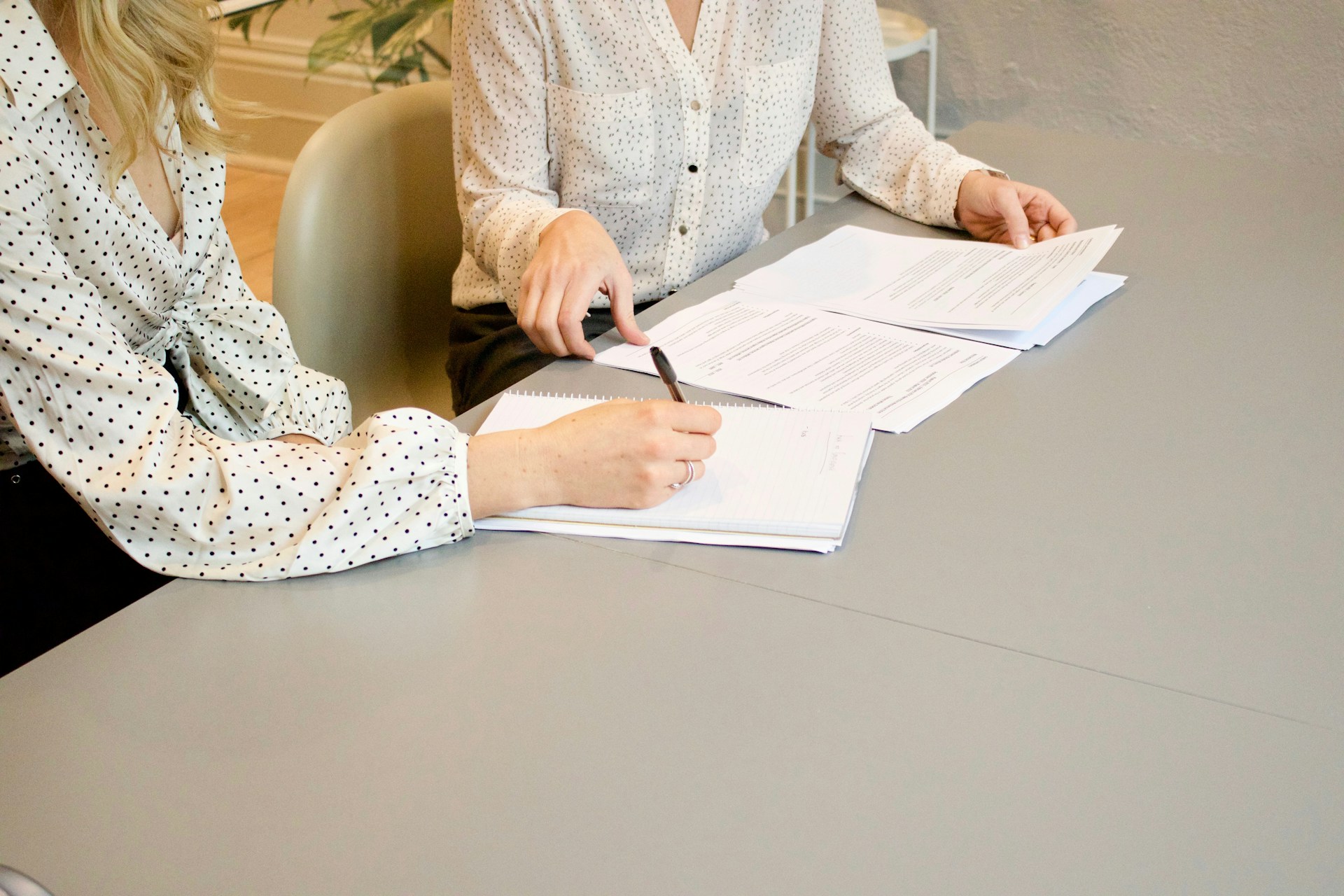 Zu sehen sind zwei Frauen, an einem Tisch mit mehreren Dokumenten vor sich