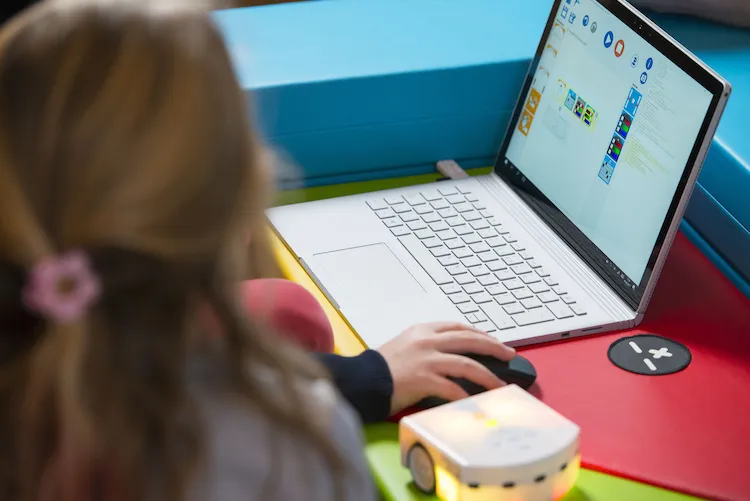 Zwei Kinder sitzen an einem Laptop. Daneben liegt ein Thymio Roboter.