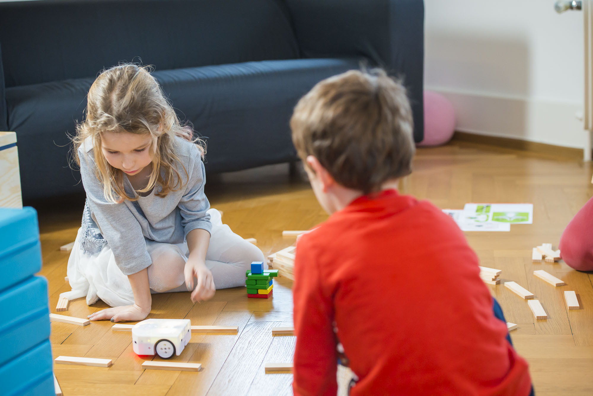 Zwei Kinder spielen mit dem Thymio Lernroboter auf dem Boden und lassen diesen durch einen Parcours fahren.