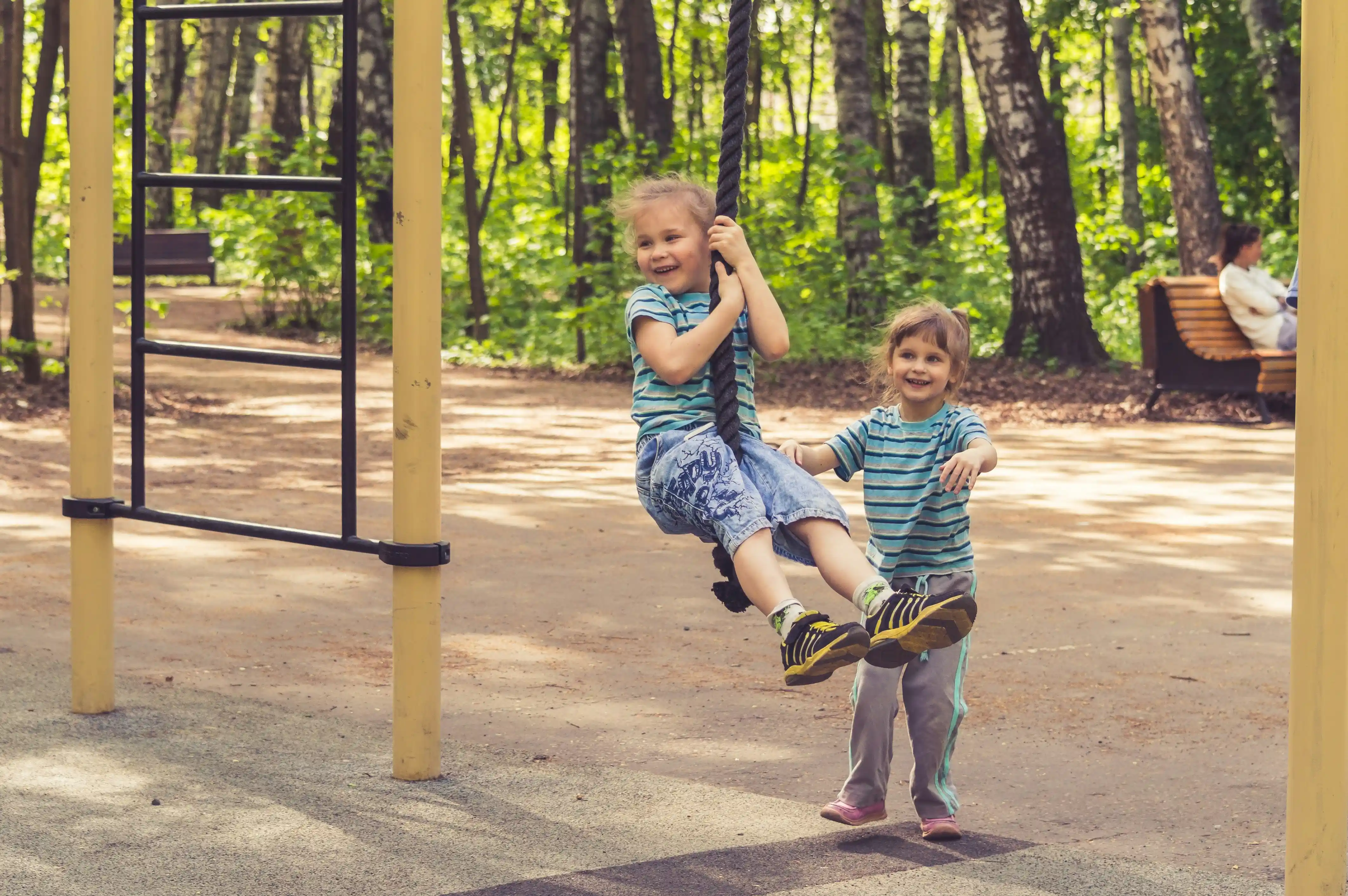 Zwei Kinder spielen auf einem Spielplatz. Eines sitzt auf einer Seilbahn.