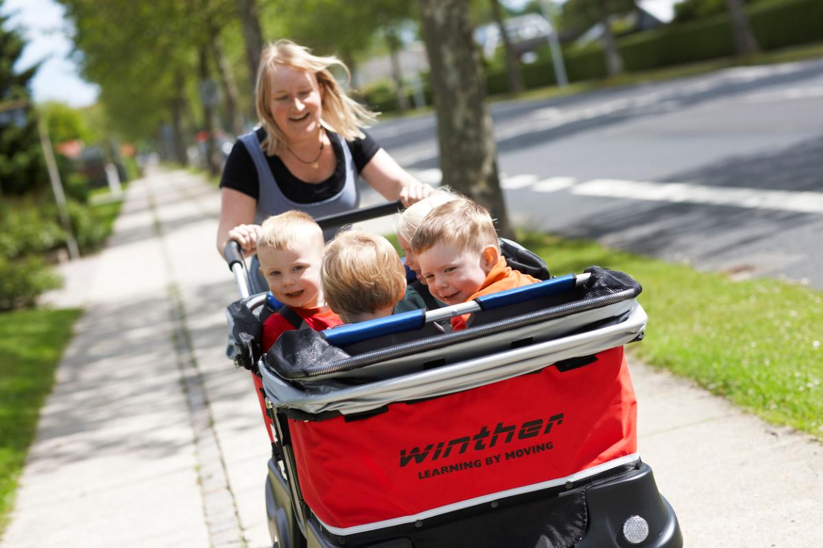 Eine Frau schiebt drei Kinder in einem roten Winther Kinderbus. 