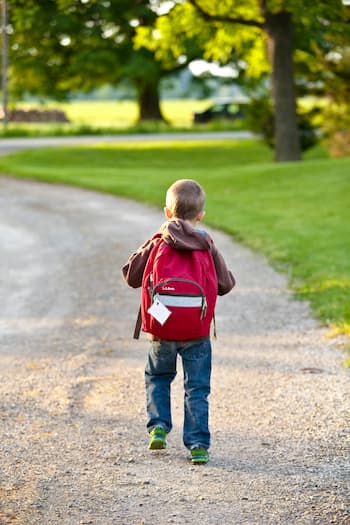 Kleiner Junge mit rotem Rucksack auf Waldweg