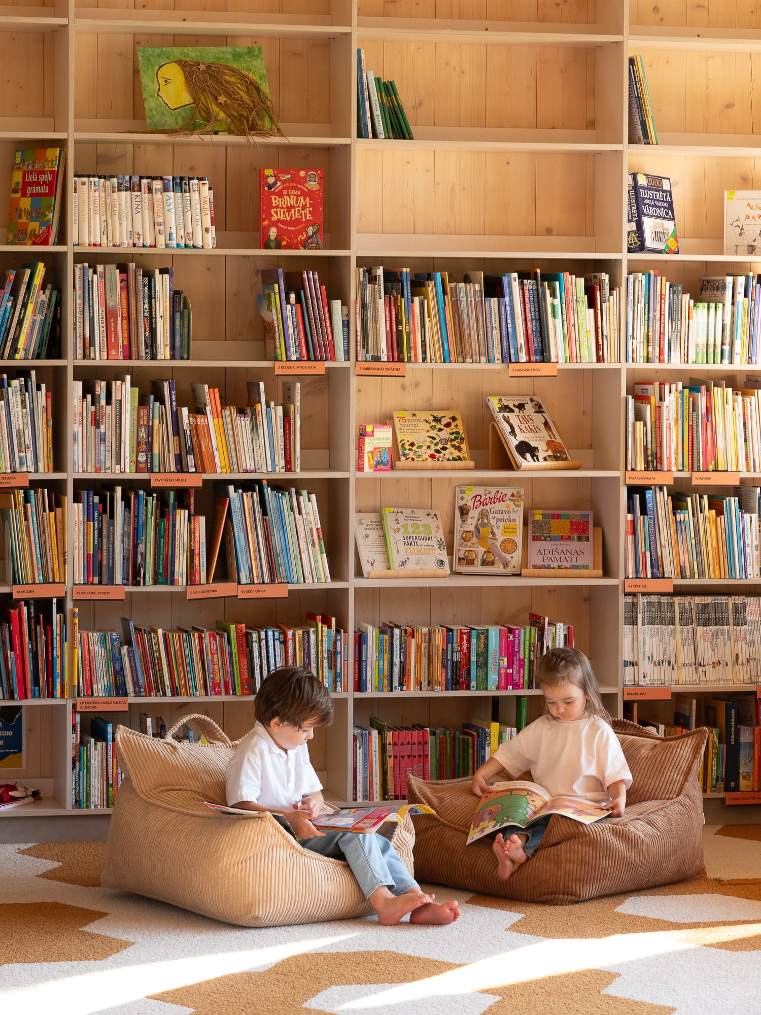 Vor einem großen Bücherregal sitzen zwei Kinder jeweils auf einem Sitzsack und lesen ein Buch