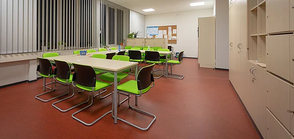 Klassenzimmer mit U-förmiger Tischkonstellation, Schrank front und grün-schwarzen Stühlen