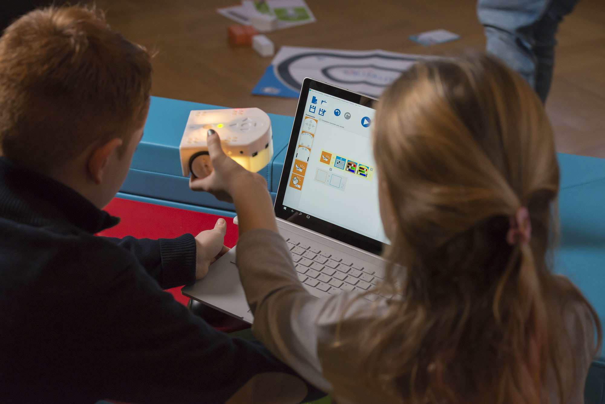 Zwei Kinder sitzen mit dem Thymio Lernroboter vor einem Laptop und programmieren diesen.