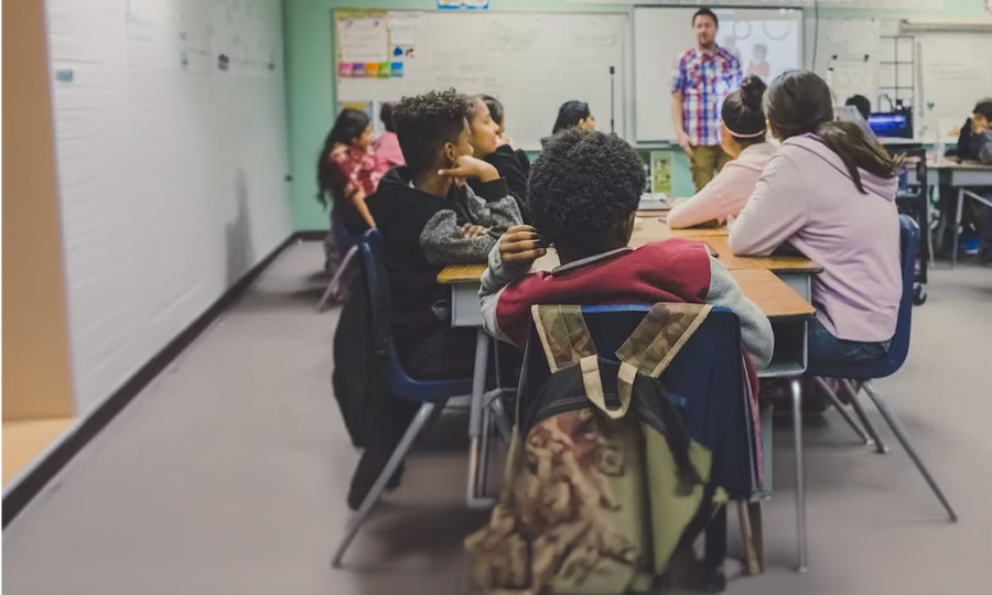 Klassenraum von hinten. Mehrere Schüler sind zu sehen und ein Lehrer steht vorne.