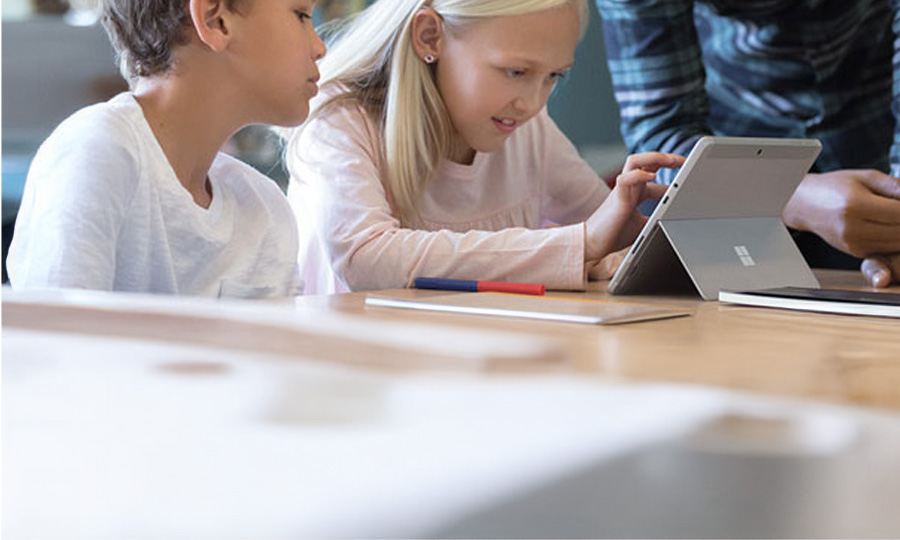 Ein Mann steht neben zwei Kindern, die an einem Microsoft Tablet arbeiten