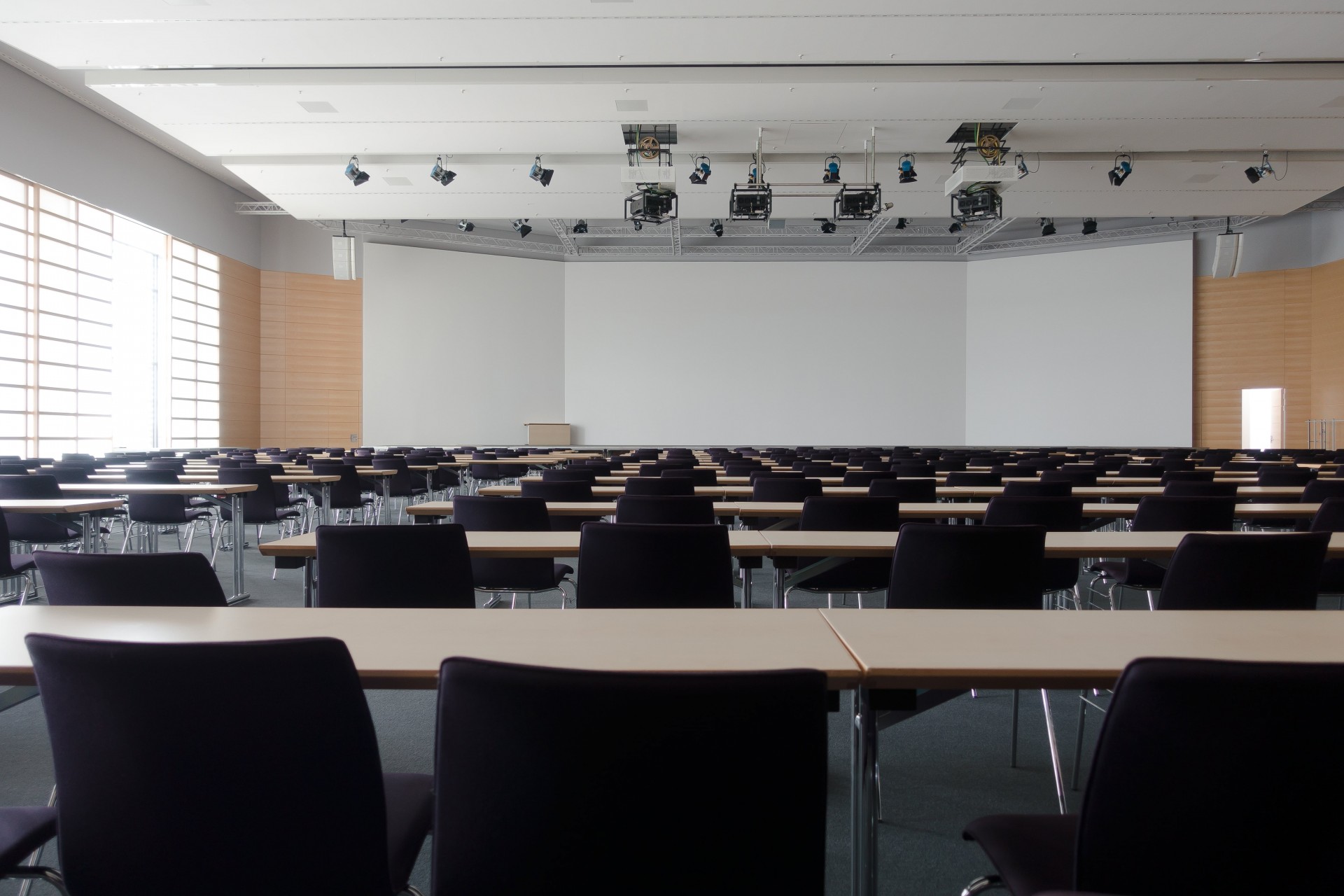 Hörsaal von hinten fotografiert. Mehrere Stuhl und Tischreihen vorneweg