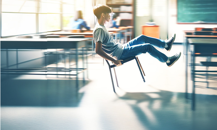 Ein Junge sitzt in einem Klassenraum und kippelt mit seinem Stuhl