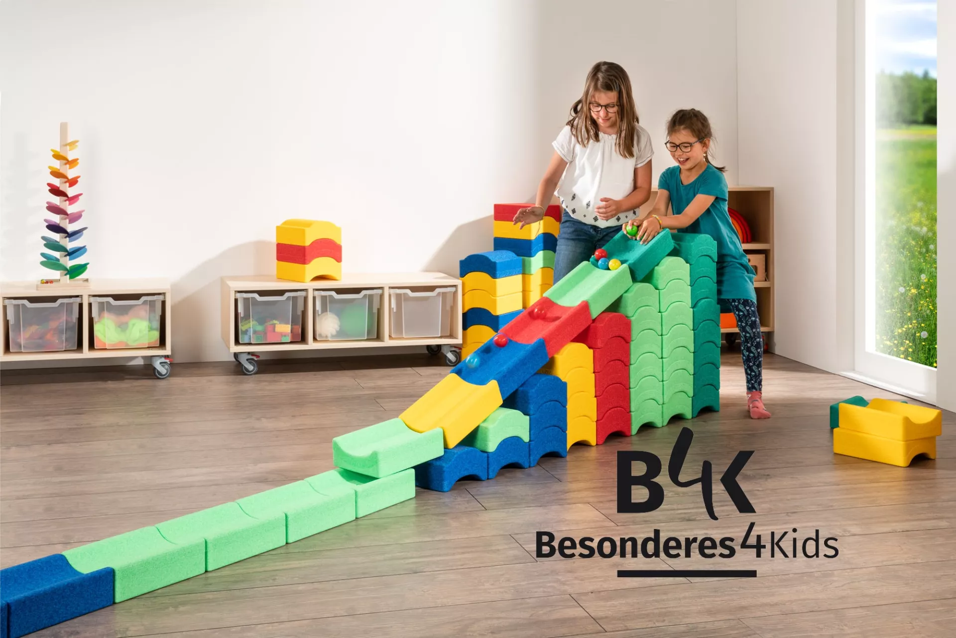 Zwei Mädchen bauen aus großen Bausteinen ein Rampe für Kugeln.In der Ecke des Bildes ist ein Logo von Besonderes4Kids