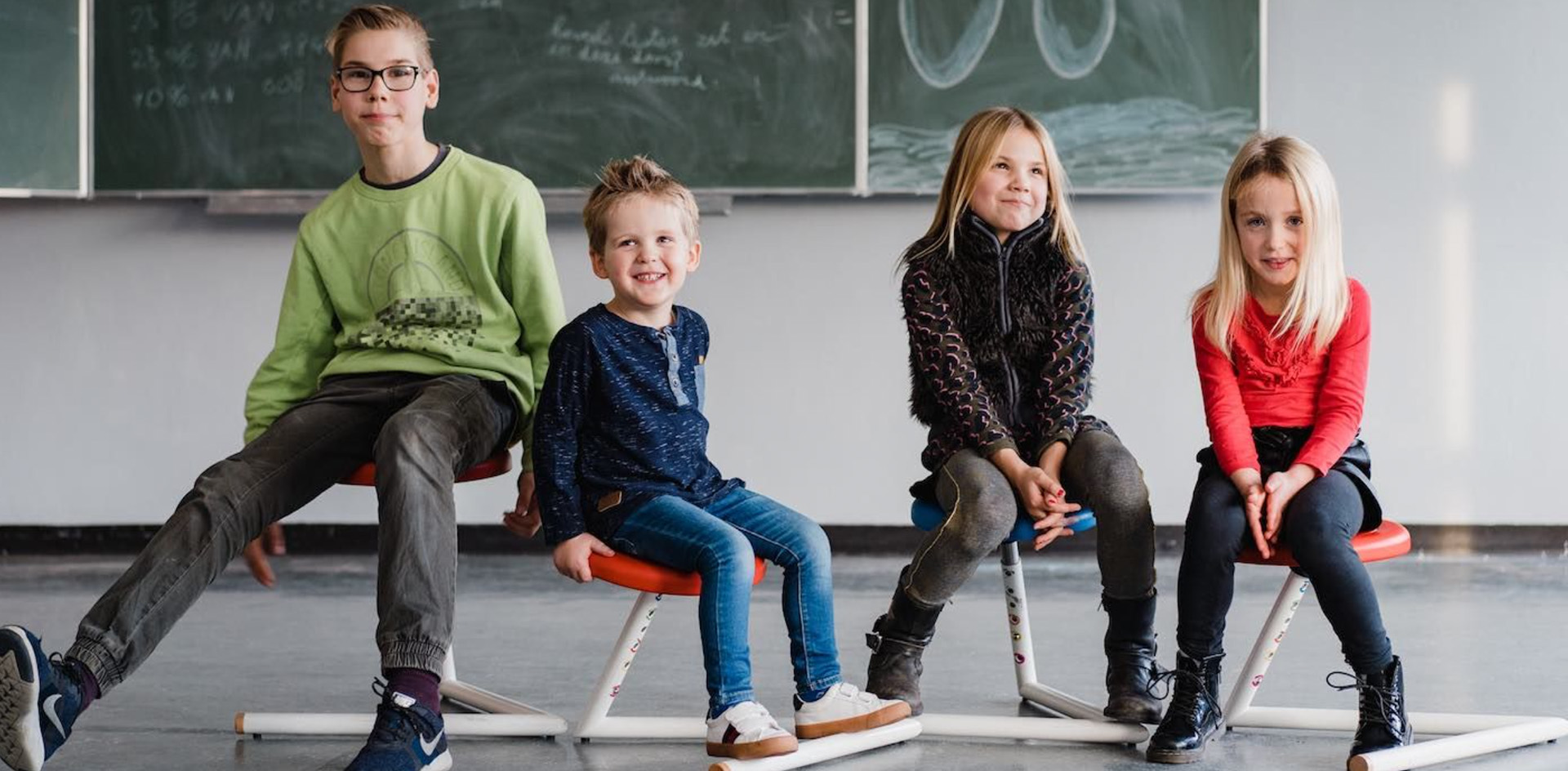 Vier Kinder sitzen nebeneinander auf einem ergonomischen Hocker