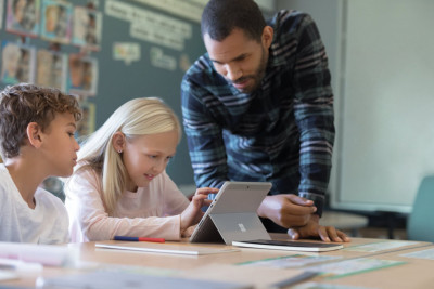 Ein Mann steht neben zwei Kindern, die an einem Microsoft Tablet arbeiten