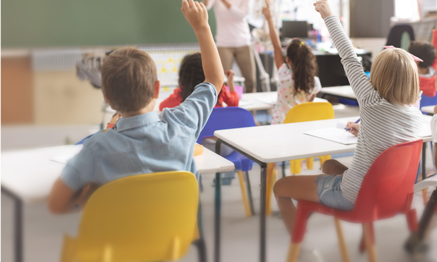 Unterrichtssituation in einem Klassenraum. Viele Kinder zeigen auf.