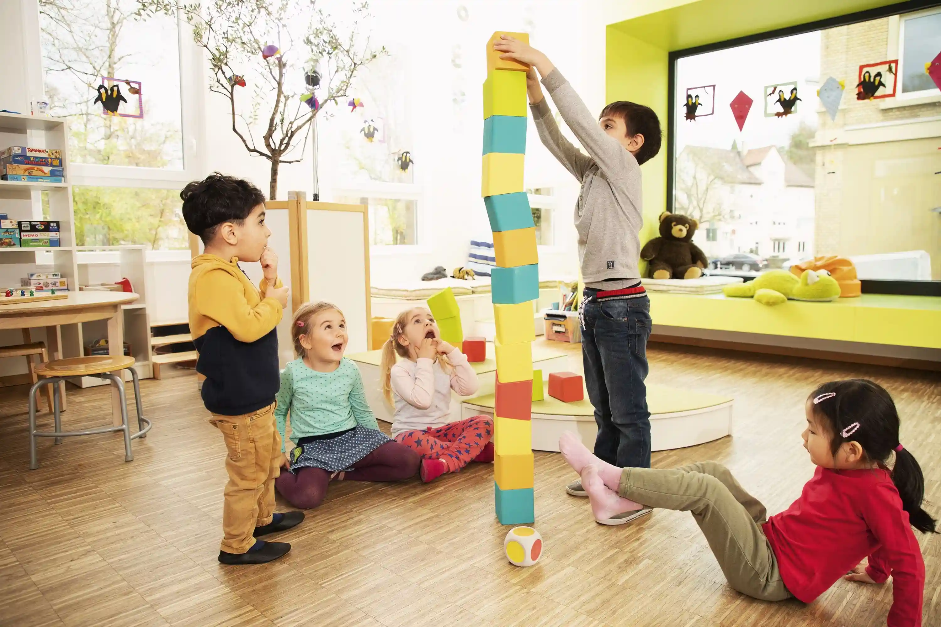 Fünf Kinder spielen auf dem Boden und bauen einen Turm aus Bauklötzen.