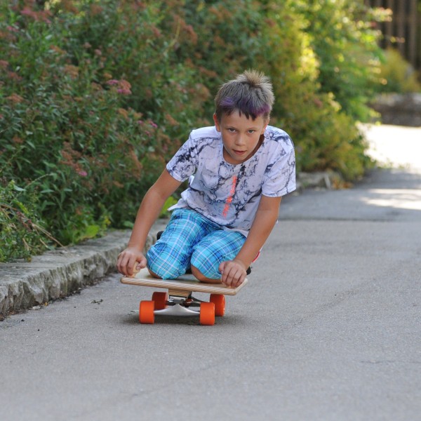 Kind fährt auf Pedalo Rollbrett Skate eine Straße herunter