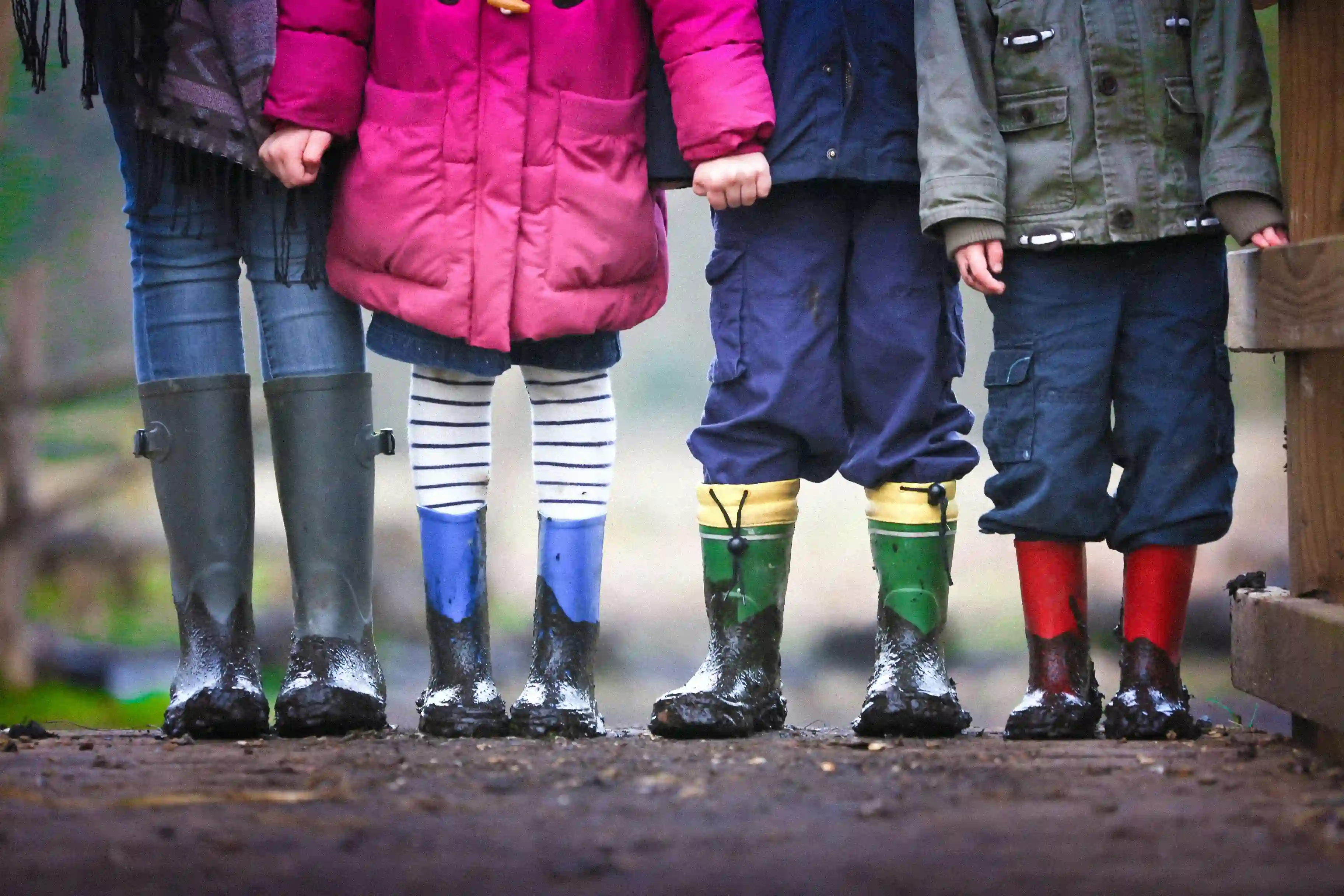 Vier Kinder stehen nebeneinander in Regenkleidung. Die Oberkörper sind nicht zu sehen.